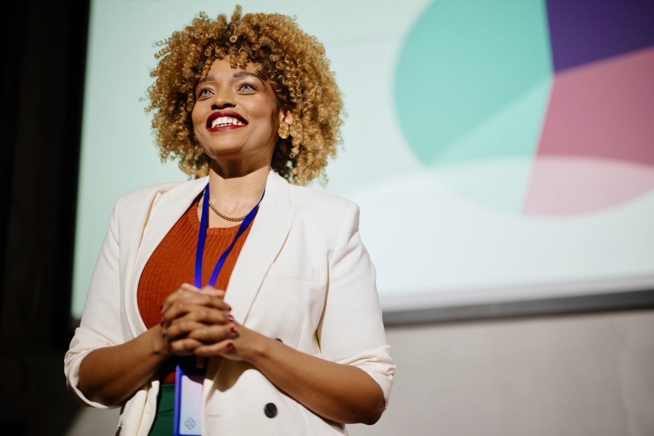 Woman in a blazer smiling onstage at a business conference