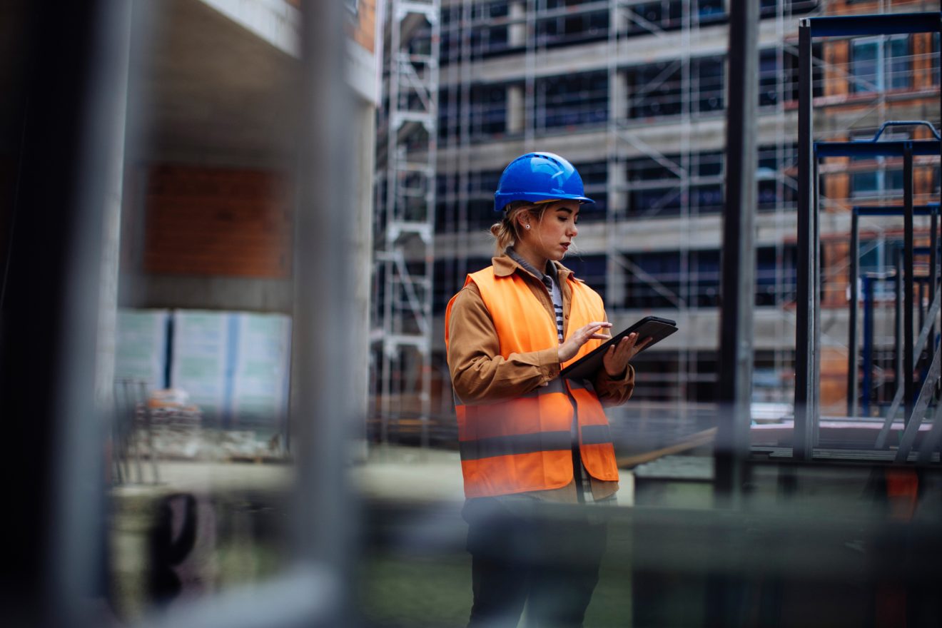 Woman in a safety vest and hardhat using a tablet on a construction site