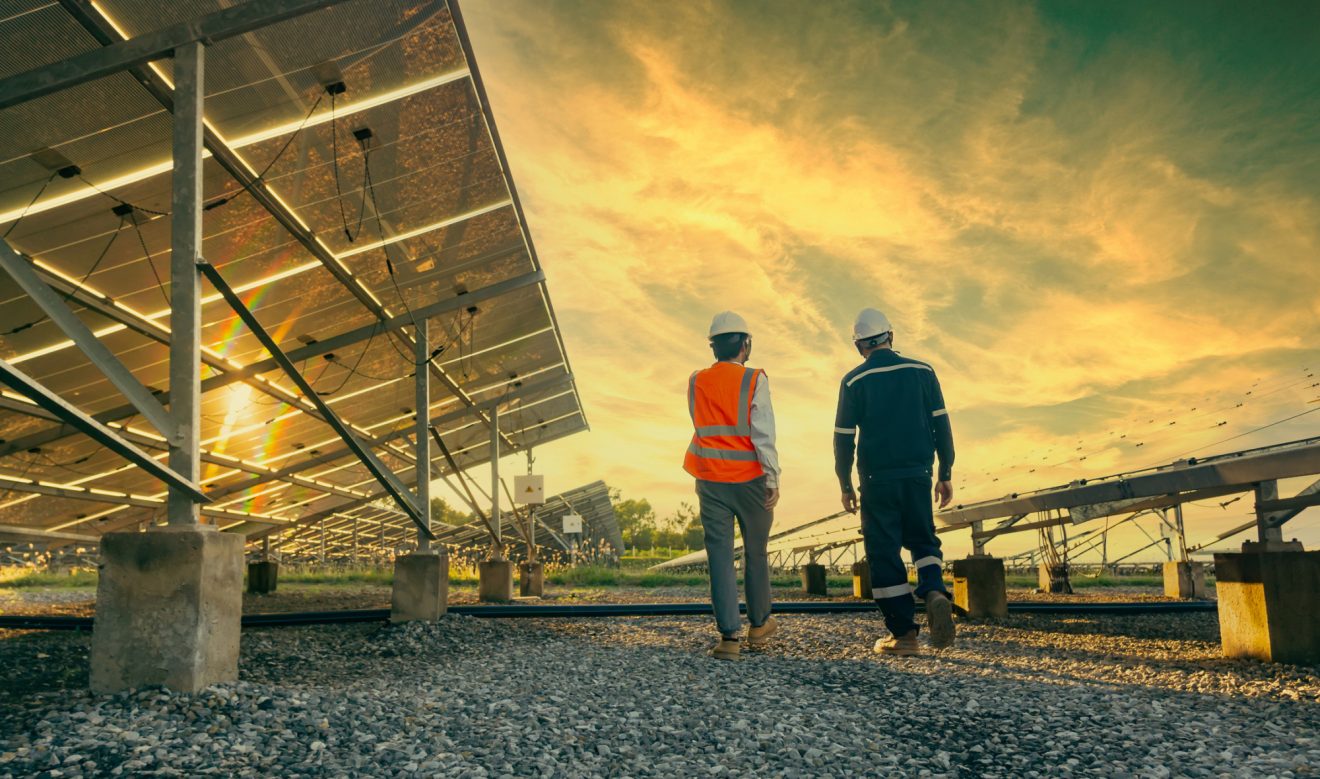 Two people in hardhats walking past solar panels