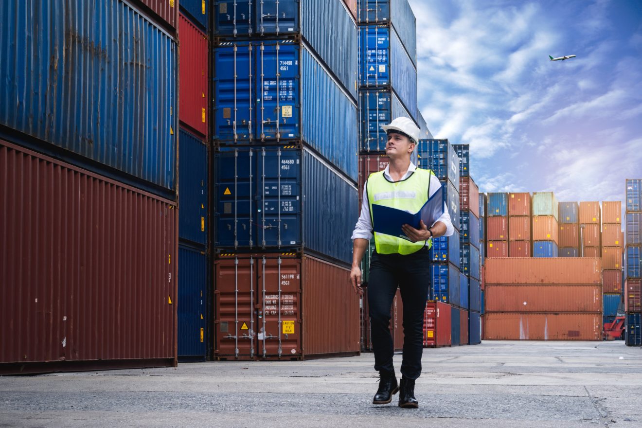 Man in a hardhat and yellow vest looking up at shipping containers