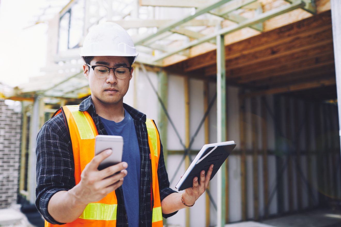 A man references a smartphone and a tablet at a construction site