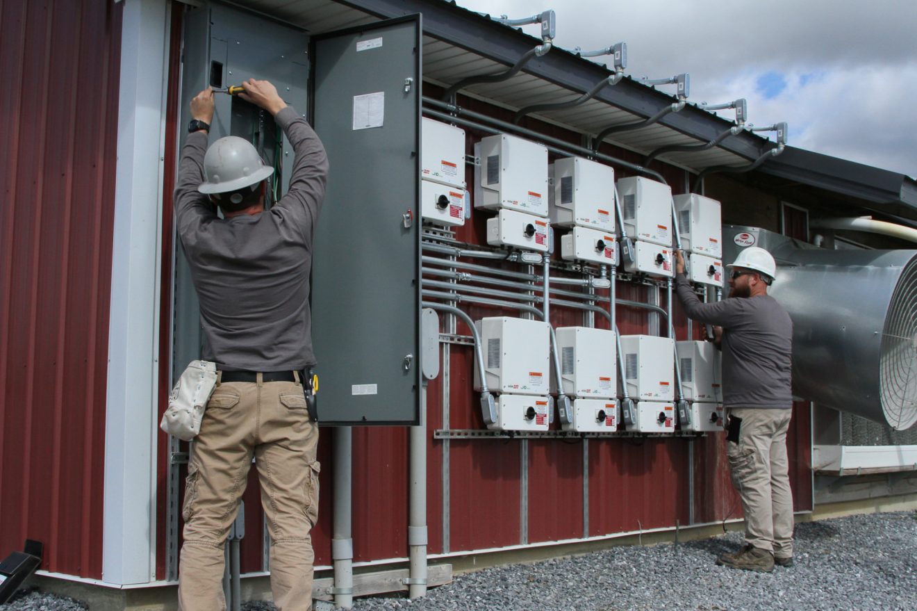 A pair of workers inspecting a series of solar control boxes.