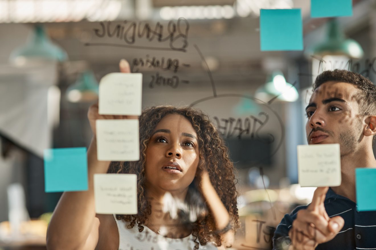 Man and woman in office collaborating on project by using sticky notes on a screen