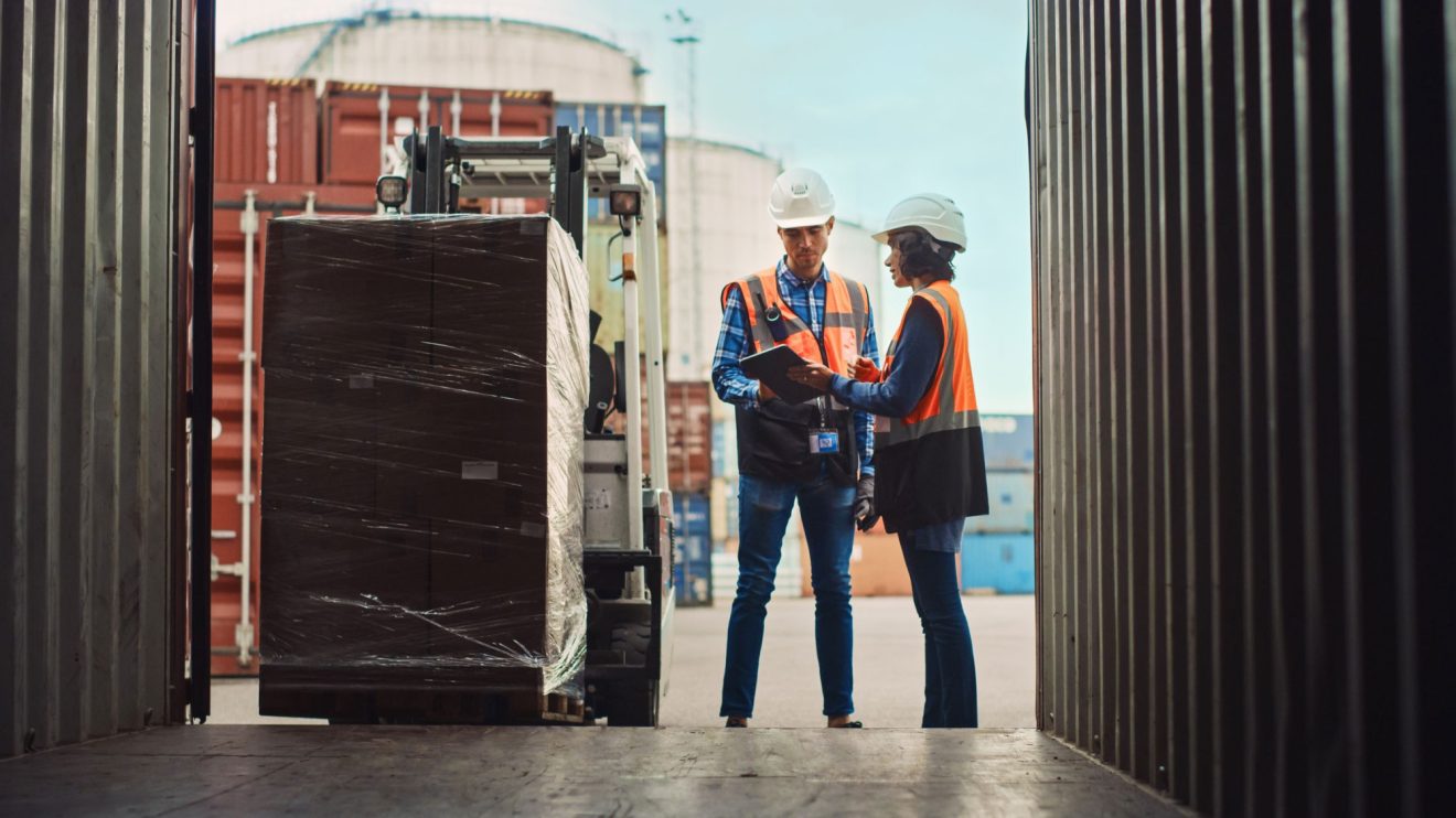 Two people discuss a forklift carrying a large box