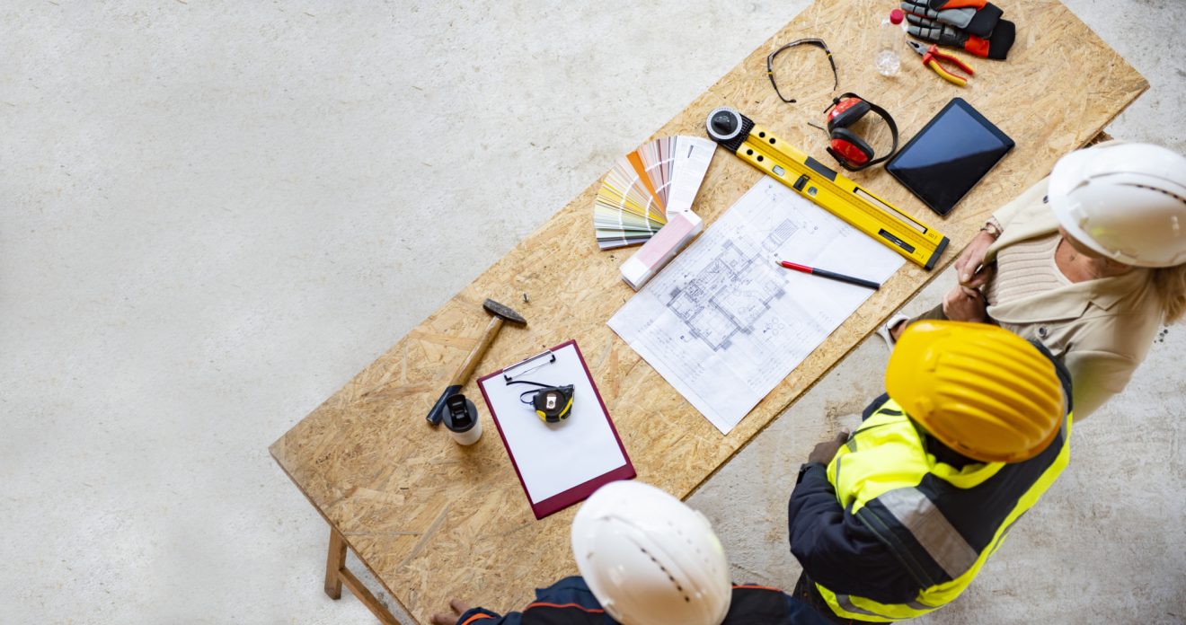 A bird's-eye view of three people looking at the blueprint on their desk at a worksite