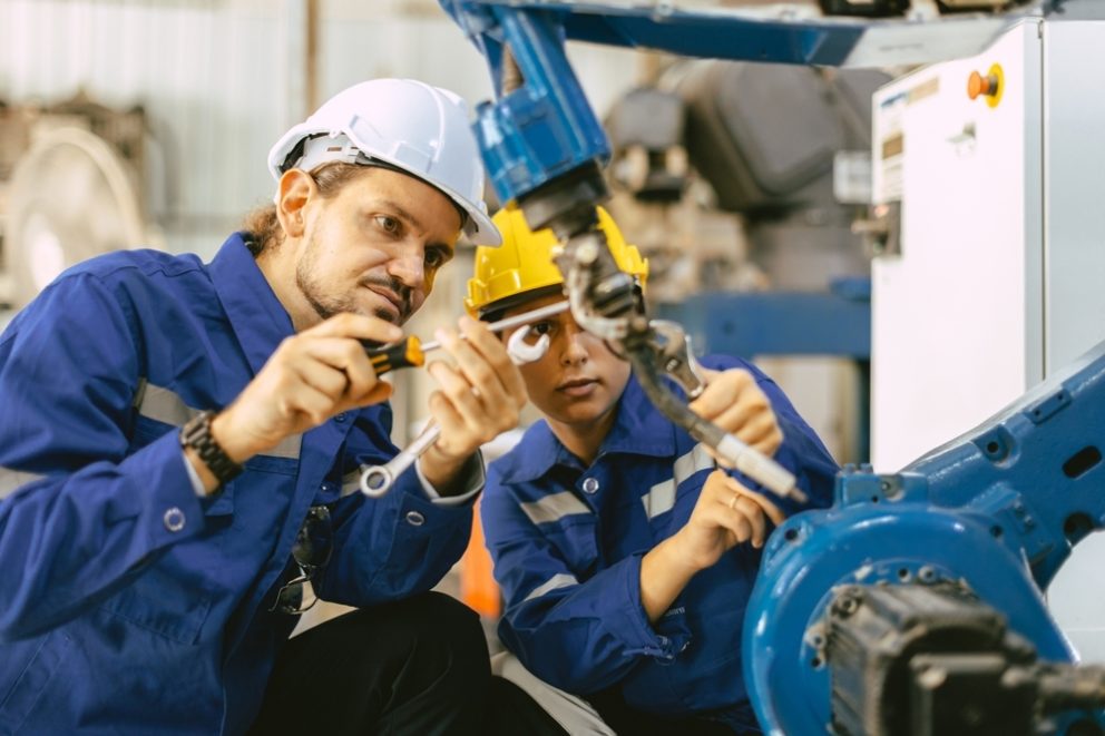 An engineer fixing a broken part of an automatic industry robotic welding arm.