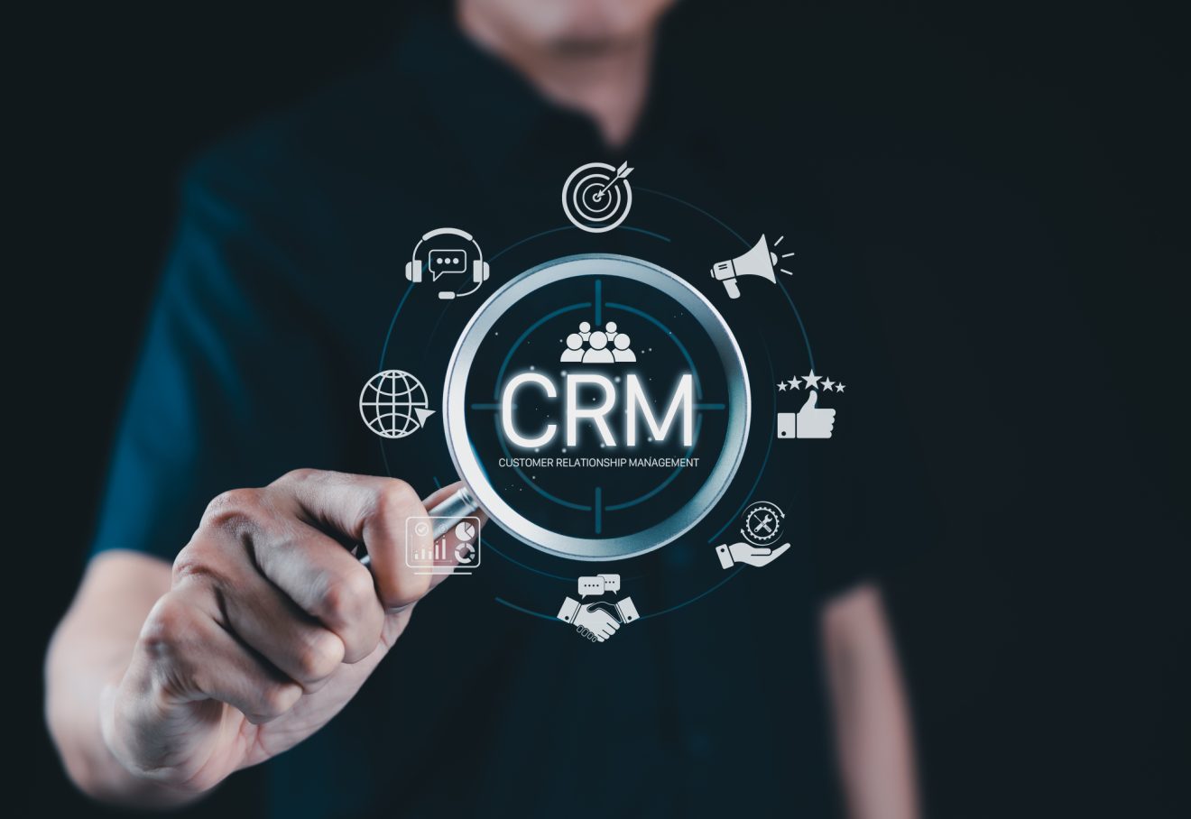 Worker holds a magnifying glass over a digital image of CRM logos