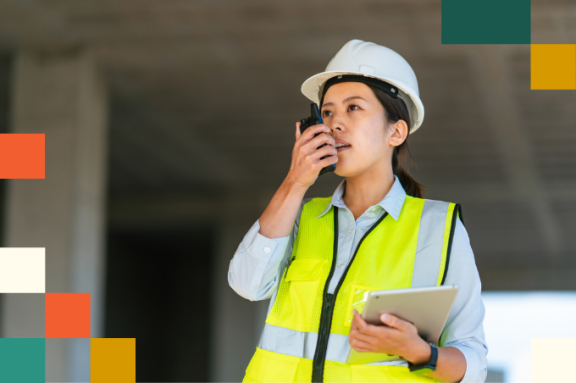 young woman in hard hat and reflective vest talking on walkie talkie