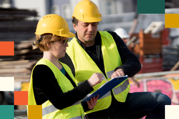 Civil engineers, a man and a woman, wearing safety jackets and helmets, checking projects on construction site