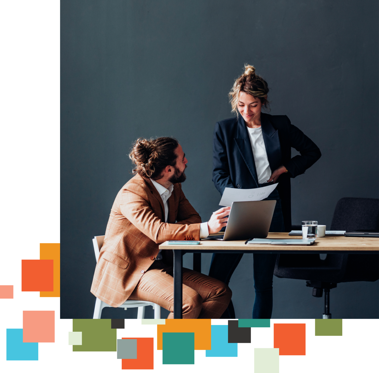 Two people reference papers and a laptop together